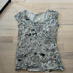 Vit och svart t-shirt med grafiskt mönster från Cheap Monday - Säljer en vit & svart t-shirt från Cheap Monday i storlek medium med svart, detaljerat grafiskt mönster över hela tröjan. T-shirten har korta ärmar och rund halsringning. Perfekt för dig som gillar unika prints!