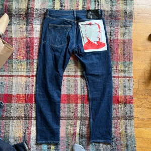 Calvin Klein Jeans Andy Warhol designer by raf simons  - Unika blå jeans från Calvin Klein Jeans Andy Warhol-kollektionen designade av raf Simons med ett stort tryck av Andy Warhol i rött och vitt på bakfickan. Klassisk femficksmodell med raka ben och svarta läderpatch bak i midjan.