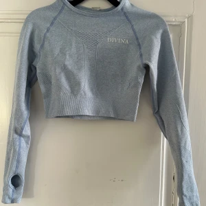 Ljusblått träningssett från Divina - Säljer ett ljusblått träningssett från Divina. Tröjan har tumhål i ärmsluten och ett snyggt mönster i tyget samt öppen detalj i ryggen. Perfekt för gymmet eller yoga! 