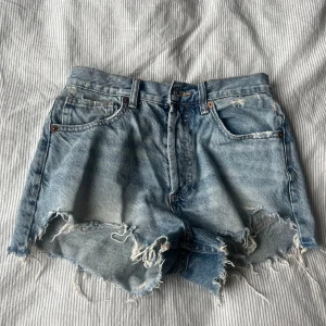 Ljusblå jeansshorts med fransar från Zara - Säljer ett par ljusblå jeansshorts från Zara med fransade kanter. Klassisk femficksmodell med mid midja och knappgylf. Perfekta för sommaren. Köpte dom sommaren 2023 men andvände dom endast under den sommaren. 