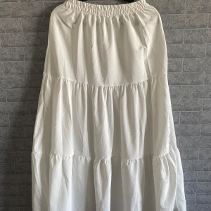 Vit långkjol med volanger - Säljer en superfin vit långkjol med volanger och resår i midjan. Kjolen har en luftig och flowy känsla, perfekt för varma dagar. Enkel att styla med både sneakers och sandaler för en chill look. Jag är 170cm och när jag har den lågmidjat så går den ner till mina fötter 🌸strlk xs-m pga resår i midjan, helt ny oanvänd köpt utomlands 