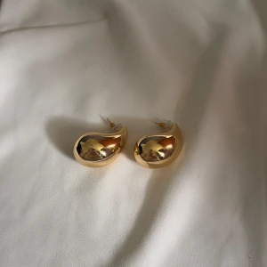 Chunky droppformade örhängen i guld - Säljer ett par chunky örhängen i droppform med spegelblank guldfinish. De är statement och har en modern, rundad design som verkligen syns. Perfekta för dig som vill ha något unikt och trendigt i smyckeslådan.