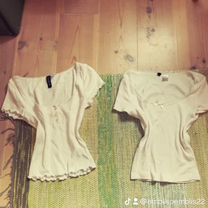 Vit ribbad topp med knappar Divided XS - Supersöt vit ribbad topp från Divided med korta ärmar, knappar framtill och volangkant nertill. Urringad hals med spetsdetalj ger en romantisk vibe. Perfekt för dig som gillar en feminin och trendig look. Den med rosetten är i xxs och den andra xs, säljer båda för 60 eller en för 40