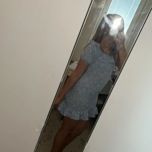 Blå blommig volangklänning Gina Tricot - Supersöt blå kortklänning från Gina Tricot med vita blommor, volang vid axlar och nederkant. Klänningen är större än vad man tror, jag är 160cm lång och klänningen är i storlek 146/152🙌 Pris kan diskuteras