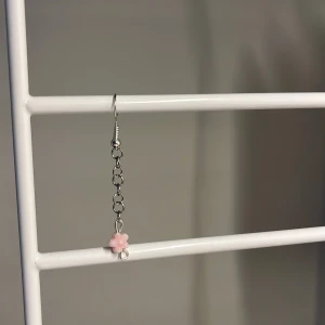 Silverfärgat örhänge med rosa blomma - Ett långt, hängande örhänge i silverfärg med kedja och en liten söt rosa blomma längst ner. Perfekt för dig som gillar unika och gulliga accessoarer med en touch av pastell. Egen gjord!