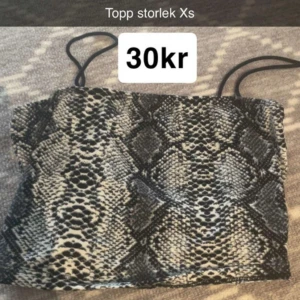 Tubtopp med ormmönster XS - Säljer en snygg tubtopp med svart och beige ormmönster. Toppen är ärmlös och har smala axelband, perfekt för att sticka ut med en cool look. Passar dig som gillar djurmönster och vill ha något trendigt i garderoben.