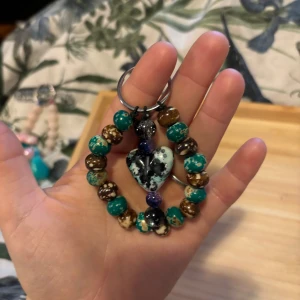 Färgglatt nyckelring med hjärta - Unikt armband med pärlor i turkos, brunt och svartvitt, dekorerat med ett hjärtformat hänge i mitten. Pärlorna har coola mönster och olika färgskiftningar som gör armbandet riktigt speciellt. Perfekt accessoar för dig som gillar färg och personliga detaljer.