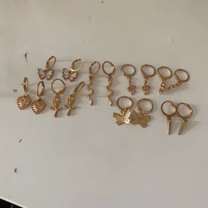 Guld örhängen det - Säljer ett set med 8 par guldiga örhängen i olika former: fjärilar, hjärtan, rosor, ormar, spikes och vågiga hängen. Några fjärilar har vit emalj, resten är helguldiga. Perfekt för dig som vill mixa och matcha coola och söta detaljer i din stil.❤️Aldrig använda! Perfekt som present eller gåva💕