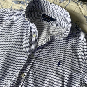 Randig skjorta Polo Ralph Lauren M - Klassisk vit och blå randig skjorta från Polo Ralph Lauren i slim fit. Skjortan har långa ärmar, knappar framtill och broderad logga på bröstet. Tillverkad i mjuk bomull och passar perfekt till en clean och stilren look. Köpt på Vinted, inga defekter som jag vet om. Vid frågor eller funderingar skicka ett meddelande💫