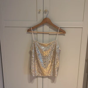 Guldig paljettopp från H&M - Ny, ej använd och prislappen sitter kvar. Glittrig topp från H&M med tunna axelband med paljetter i guld. Croppad modell. 