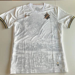 Vit AIK x Nike fotbollströja Stockholm - AIK fotbollströja replika i vitt med subtilt grått stadsmotiv över hela framsidan. Guld- och svartdetaljer på ärmsluten, AIK-emblem på bröstet och Nike-logga i guld och svart. Tillverkad i lätt och ventilerande funktionsmaterial. Endast handtvätt gäller.