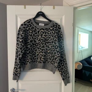 Grå leopardmönstrad stickad tröja Zara - Säljer en grå stickad tröja från Zara med svart leopardmönster. Tröjan har rund halsringning, ribbade muddar och lång ärm. Perfekt för dig som vill sticka ut med ett djurmönster och ändå hålla det stilrent.