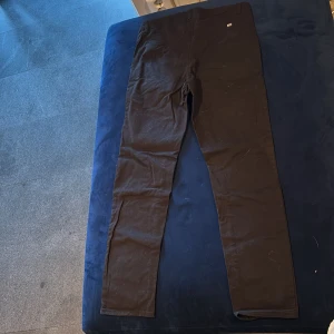 Svarta slim fit chinos från H&M - Svarta chinos från H&M i slim fit-modell med justerbar midja. Byxorna har klassisk design med fickor fram och bälteshällor. Perfekta för dig som gillar en smalare passform och stilren look.