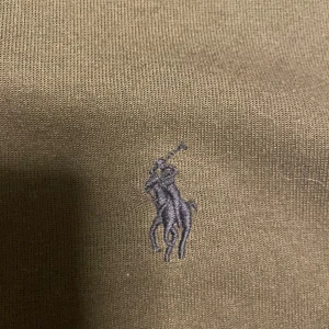 Olivgrön pikétröja från Ralph Lauren - Snygg olivgrön pikétröja från Ralph Lauren med klassisk broderad logga på bröstet. Tröjan är i mjuk bomull och har en stilren look som passar perfekt till jeans eller chinos.