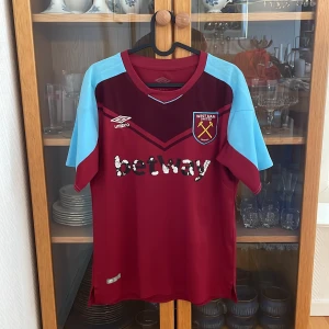 West Ham United hemmaställ Umbro 2017-2018 size M - Säljer en officiell West Ham United fotbollströja från Umbro. Tröjan är vinröd med ljusblå korta ärmar, klubbmärke broderat på bröstet och sponsortryck på magen. Tillverkad i lätt och ventilerande polyester, perfekt för match eller träning. Utöver sponsor trycket på magen är varan i väldigt gott skick! 