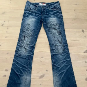 Blå Miss Sixty jeans med broderi - Unika lågmidjade blå jeans från Miss Sixty med broderade detaljer och slitningar på både fram- och baksida. Byxorna har bootcut-modell och coola svarta broderier med blommönster och paljetter.  Ursnygga jeans som jag säljer för de är för små på mig😔 storlek 27!!