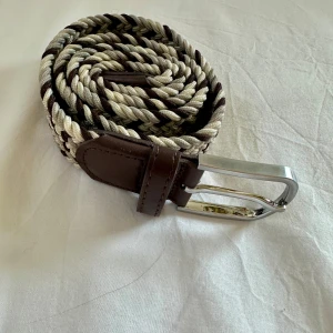 Flätat bälte från Onewear  - Snyggt flätat bälte från Onewear  i beige och brunt med detaljer i mörkbrunt skinn. Bältet har ett silverfärgad metallspänne. Perfekt accessoar för att lyfta din outfit.
