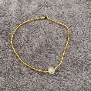 Guldigt pärlfotlänk med kubpärla - En fotlänk med små guldfärgade pärlor och en större kubformad pärla i mitten som skimrar i regnbågens färger. Fotlänken har en enkel och trendig design som passar perfekt till din stil.