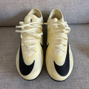 Nike Mercurial Air Zoom fotbollsskor - Snygga Nike Mercurial Air Zoom fotbollsskor i ljusgul med svarta detaljer och stor Swoosh-logga. Skorna har snörning, platt sula med dobbar och är tillverkade i syntetmaterial för bästa grepp och lätt känsla på planen. Perfekta för dig som vill sticka ut på fotbollsplanen.