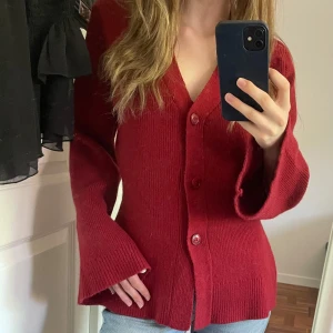 Röd stickad, figursydd kofta med vida ärmar - Mysig röd stickad kofta med v-ringning och stora knappar framtill. Koftan har långa, vida ärmar och är figursydd