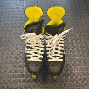 Bauer inlines i svart och gul - Snygga Bauer inlines med svart och gul design, vita snören och robust yttermaterial. Utrustade med Hi-Lo hjul och detaljer i silver. Insidan är fodrad i gult och svart för extra komfort. Perfekta för dig som vill ha fart och stil på gatan.