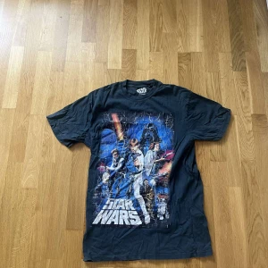 Svart Star Wars t-shirt XS - Cool svart t-shirt från Star Wars med stort tryck av klassiska karaktärer och logga på framsidan. T-shirten har korta ärmar, rund hals och en loose fit. Perfekt för dig som älskar sci-fi och vill sticka ut med en ikonisk look.