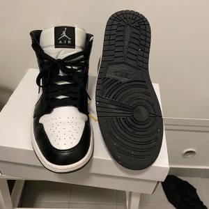 Nike Air Jordan 1 Mid svart/vit - Nike Air Jordan 1 Mid sneakers i svart och vitt skinn. Klassisk high-top siluett med svart swoosh, perforerad tå och svart snörning. Ikonisk Jumpman-logga på plösen och Air Jordan Wings på sidan. Perfekta för dig som vill sticka ut med en tidlös streetstyle. Pris kan diskuteras och skorna är i storlek 41 