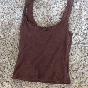 Brun ribbad linnetopp från H&M Divided - Supersöt brun ribbad linnetopp från H&M Divided i storlek XXS. Toppen har spetskant runt urringningen och en liten rosett framtill. Perfekt för lager-på-lager eller till jeans. Mjuk och stretchig känsla.