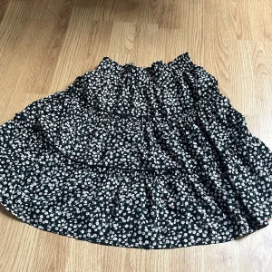 Blommig svart kjol från SHEIN - Supersöt svart kjol från SHEIN med små vita och rosa blommor. Kjolen har volanger och resår i midjan för en bekväm passform. Perfekt för dig som gillar en feminin och trendig stil.