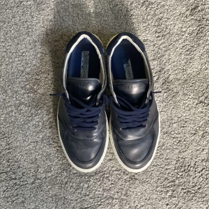 Mörkblå sneakers från Jacob Cohen - Snygga mörkblå sneakers från Jacob Cohen med klassisk design. Skorna har ovandel i skinn, vita sulor och mörkblå snörning. Insidan är fodrad i vitt och blått, och tån är rundad. Perfekta för dig som gillar stilrena och tidlösa sneakers. Skickas i orginalbox, med alla orginalgrejer. Byten går också bra!