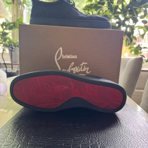 Mörkblå sneakers från Christian Louboutin - Snygga mörkblå sneakers från Christian Louboutin i mocka med klassisk röd sula. Skorna har rund tå, snörning och diskret broderad logga på hälen. Perfekta för dig som vill ha en lyxig och stilren look med en ikonisk touch kan sänka priset vid snabb affär storlek 42 lådan och allt följer med 