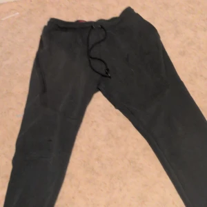 Svarta mjukisbyxor från Nike M - Svarta mjukisbyxor från Nike i storlek M. Byxorna har dragsko i midjan, fickor med dragkedja och Nike-logga på benet. Perfekta för chill eller träning, mjukt material och klassisk look.