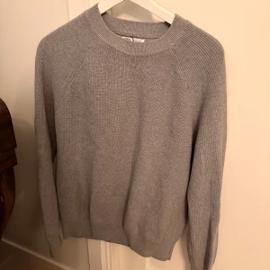 Grå stickad tröja från Zara - Säljer en stilren grå stickad tröja från Zara i storlek S. Tröjan har rund halsringning, ribbade muddar och lång ärm. Perfekt för lager-på-lager och enkel att matcha med jeans eller kjol. Supermjuk och skön att bära under kyliga dagar.