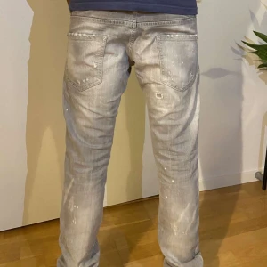 Ljusgrå slitna jeans från Dsquared - Säljer ett par ljusgrå jeans från dsquared med coola slitningar och trasiga detaljer på både fram- och baksida. Jeansen har raka ben, klassiska fickor och en röd dsquared-tag vid fickan.