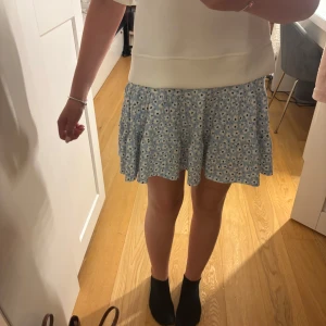 Blommig blå kortkjol med volang - Supersöt blå kortkjol med vita blommor och volangkant. Priset går att diskutera!❤️