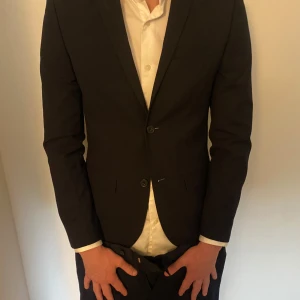 Mörkblå kostym H&M & Dressmann slim fit - Säljer en mörkblå kostym med kavaj från H&M i slim fit och matchande kostymbyxor från Dressmann, även de i slim fit. Klassisk design med två knappar på kavajen och raka byxben. Perfekt för dig som vill ha en stilren och modern look.