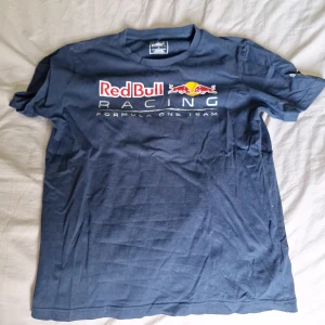 Red Bull Racing t-shirt från Puma - Mörkblå Red Bull Racing t-shirt från Puma med tryck på bröstet. Klassisk passform och korta ärmar, perfekt för dig som gillar Formel 1 och sportig stil. Tillverkad i mjuk bomull som känns skön mot huden.