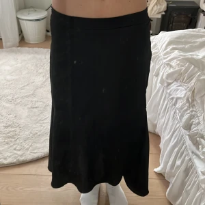 Svart satinkjol från co'couture - Säljer en svart långkjol från co'couture i glansigt satinmaterial. Kjolen har en enkel och stilren design med lätt utsvängd form och resår i midjan för skön passform. Perfekt att styla med chunky sneakers eller boots.