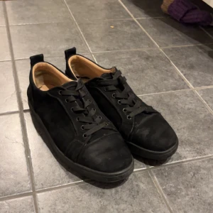 Svarta sneakers med röd sula - Snygga svarta sneakers i mocka med klassisk snörning och rund tå. Skorna har en ikonisk röd sula som sticker ut och ger en lyxig känsla. Perfekta för dig som vill ha en stilren men ändå unik look.