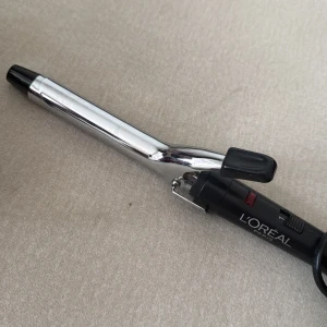 Locktång från L'Oréal Paris - Locktång i svart och silver från L'Oréal Paris med klassisk klämma och värmereglering. Perfekt för att skapa snygga lockar eller beach waves. Utrustad med lång sladd och enkel on/off-knapp. Metall och plast i stilren design.