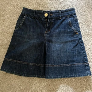 Mörk jeanskjol från Gina Tricot - Snygg mörkblå jeanskjol från Gina Tricot med klassiska fickor fram och bak, bälteshällor och dragkedja. Kjolen har en lätt A-linjeform och markerade sömmar nertill för en cool look. Perfekt till sneakers eller boots.