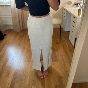 Beige linnekjol från Vero Moda - Snygg beige långkjol från Vero Moda i linneblandning. Kjolen har hög midja, resår baktill och en stilren slits framtill som ger extra edge. Perfekt för dig som gillar en clean och avslappnad look. Aldrig använd 