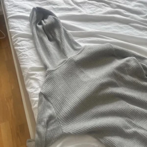 Grå ribbad hoodie från Gina Tricot - Supermysig grå ribbad hoodie från Gina Tricot i storlek S. Tröjan har dragkedja framtill, huva med snörning och långa ärmar. Den är tajt och kort, inga synliga tecken på användning förutom att den är noppig