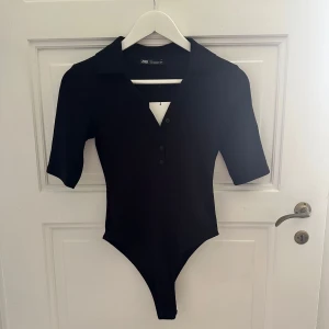 Svart body med krage från Zara - Svart body från Zara med  krage och v-ringning. Aldrig använd och med prislapp kvar. 