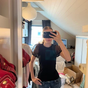 Svart blus med puffärmar från Lindex - Supersnygg svart blus från Lindex med transparenta puffärmar som ger en trendig vibe. Toppen är figurnära och har rund halsringning. Perfekt att styla med jeans eller kjol för en cool look.