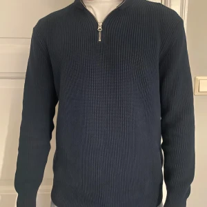 Mörkblå stickad half zip-tröja  - Mörkblå stickad tröja med half zip-dragkedja i halsen. Tröjan har ribbad struktur och lång ärm, perfekt för lager-på-lager. Snygg och enkel att matcha med jeans eller chinos.