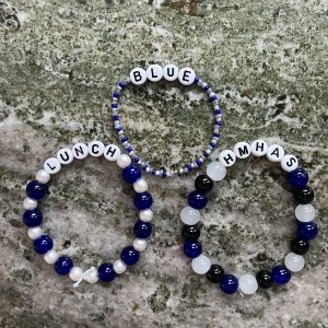 Färgglada bokstavsarmband med pärlor - Tre armband med bokstavspärlor: ett med texten 'LUNCH', ett med 'HMHAS' och ett med 'BLUE'. Armbanden har blå, vita och svarta pärlor i olika kombinationer. Perfekt accessoar för att ge din stil en personlig touch.