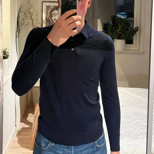 Mörkblå pikétröja från Massimo Dutti - Säljer en stilren mörkblå pikétröja från Massimo Dutti i merinoull. Tröjan har lång ärm, klassisk krage och knäppning framtill. Perfekt för dig som gillar en tidlös och enkel look. Den är i storlek M men skulle säga att passformen är mindre, där av säljer jag den.