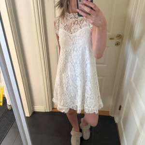 Vit spetsklänning med hög hals - Säljer en söt vit klänning i spets med hög hals och ärmlös design. Klänningen har A-linjeform och fina spetsdetaljer över hela plagget. Perfekt för sommarens tillfällen eller studentfirande. Helt ny med lappen kvar. Märket är Dry Lake Stockholm, nypris 1500. Hör av er vid eventuella frågor eller fler bilder!🥰
