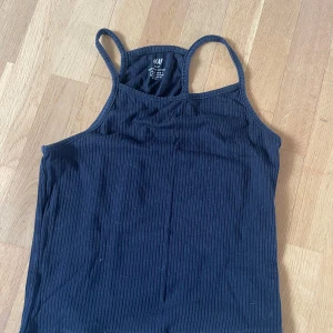 Svart ribbad linnetopp från H&M - En svart ribbad linnetopp från H&M Basic i ekologisk bomull. Toppen har smala axelband och en enkel, stilren design som passar till mycket. Perfekt för varma dagar eller som lager under andra plagg.